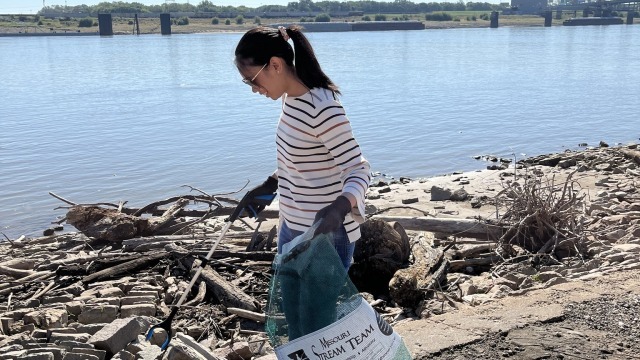A volunteer picks up trash along riverfront