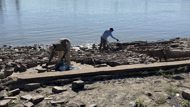 Two volunteers pick up trash along riverfront