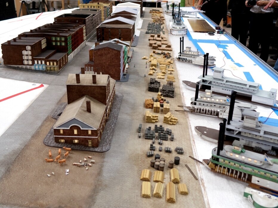 A diorama is under construction depicting buildings, people, livestock, cargo, and steamboats, allowing visitors to experience the historic riverfront era before the Gateway Arch.