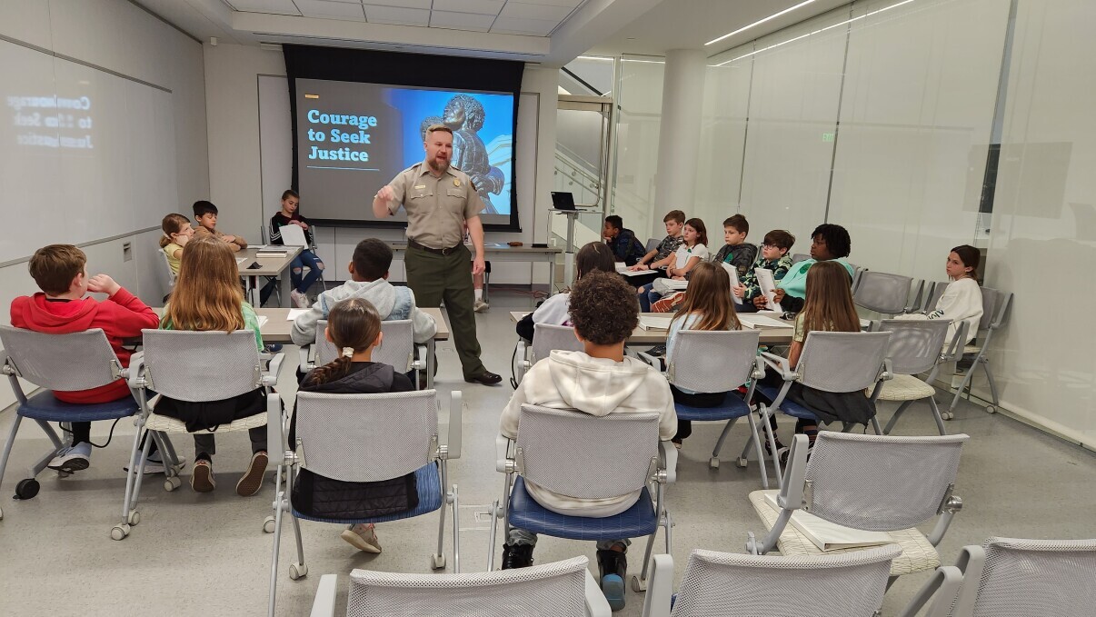 Ray Brundge speaks to a group of students in the Gateway Arch Visitor Center.